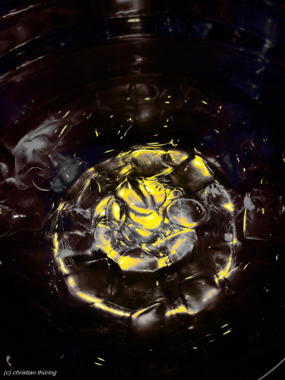 Nahaufnahme von Wasser in einem Glas mit gelben Lichtreflexen und kreisförmigen Strukturen.
