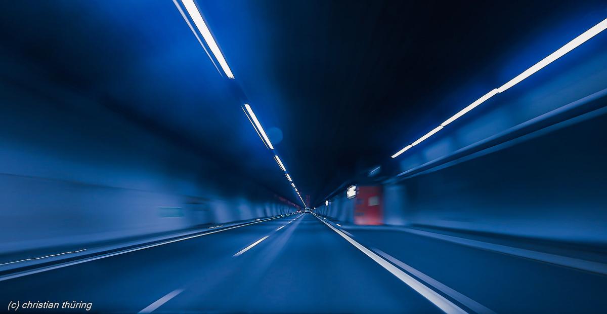 Leere Fahrbahn in einem blau ausgeleuchteten Tunnel mit Linienlichtern an der Decke.