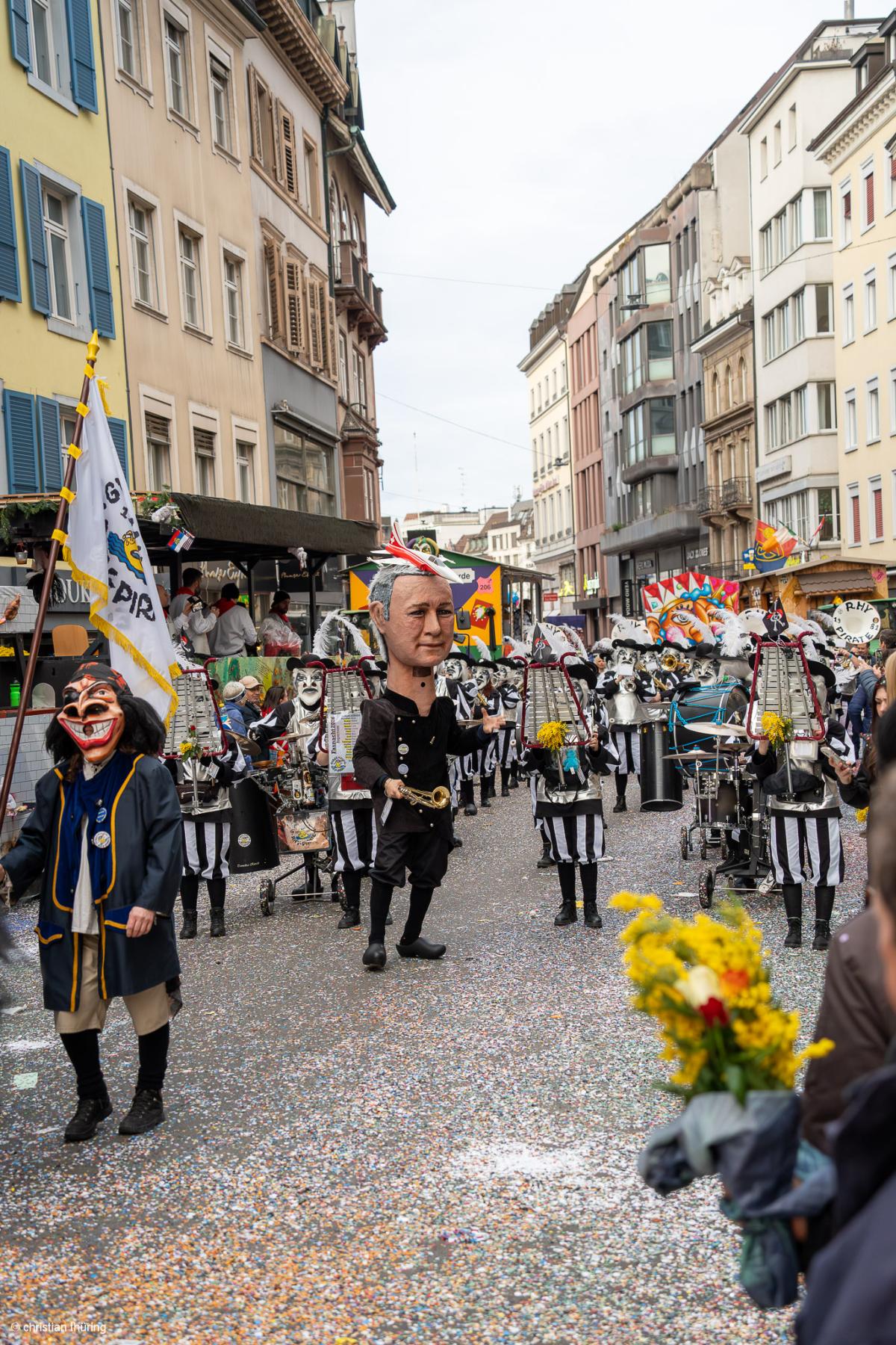 Fasnachtsgruppe mit grossen Larven, Guggemusik und Fahne in Basler Altstadt, Strassen voller Schyssdräggziigli.
