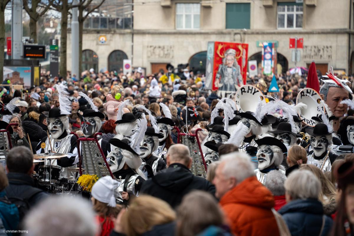 Guggemuusig rhy-pirate mit weissen Larven und Federn spielt am Fasnachtsumzug vor grossem Publikum.